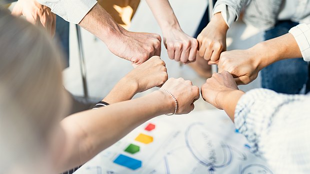 Foto von 7 Fäusten die einen Kreise bilden als Symbol für Teamarbeit